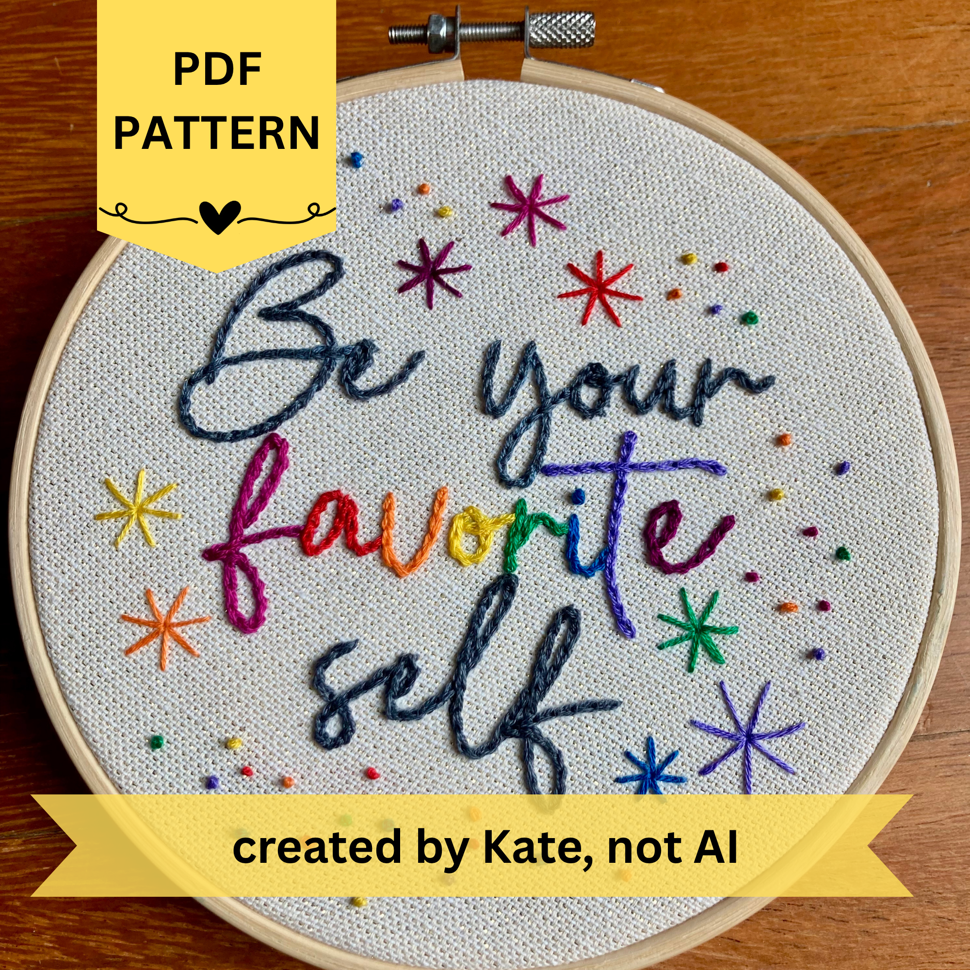 PDF Pattern created by Kate, not AI. Be Your Favorite Self is embroidered in a script font on cream fabric with gold threads woven in. Favorite is sewn in rainbow colors, and stars surround the quote. This wall art is framed in a light wood embroidery frame.