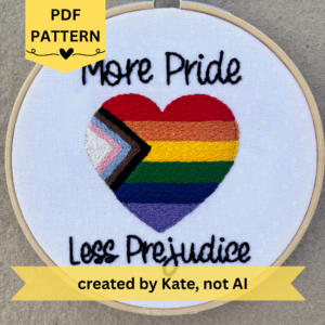 PDF pattern created by Kate, not AI. More Pride Less Prejudice. Text in script font and hand embroidered in black. Words are placed above and below a heart shaped progress pride flag. Heart flag includes white, pink, light blue, brown, black, red, orange, yellow, green, blue, and purple stripes. Fabric is white cotton with white polka dots. Framed in light wood embroidery hoop