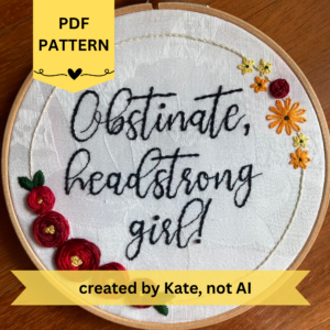 PDF Pattern created by Kate, not AI. "Obstinate, headstrong girl!" Lizzie Bennett quote in sparkle black thread with red roses and yellow and orange daisies. Fabric is white damask. Embroidery is displayed in light wood embroidery hoop