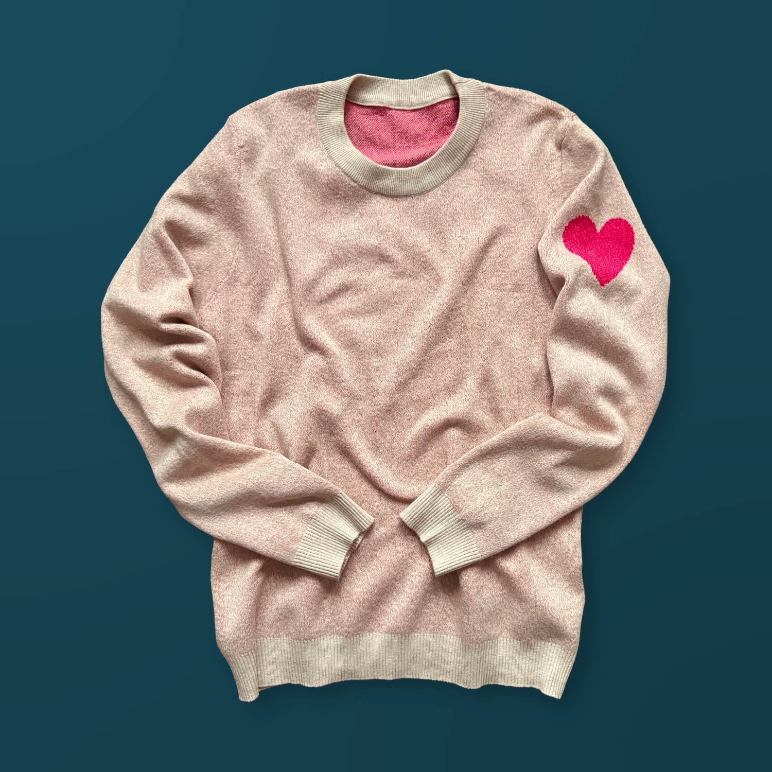 A cream color sweater with a bright red heart design on the left sleeve.