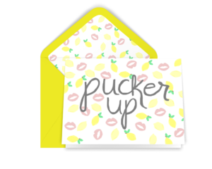 Greeting card with pattern of illustrated yellow lemons and pink lips with "pucker up" written in gray calligraphy. Yellow envelope lined with same pattern.